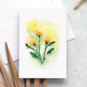 Loose yellow dandelion flowers on a greeting card overlaying white envelope on a marble background